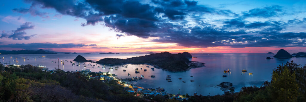 Panorama of Labuan Bajo bay at twilight with town lights, moored boats and islands