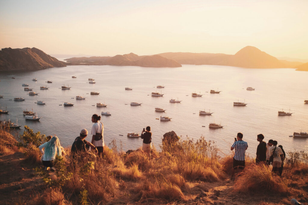 Travelers on a hilltop at sunset watching the moored fleet in Labuan Bajo bay