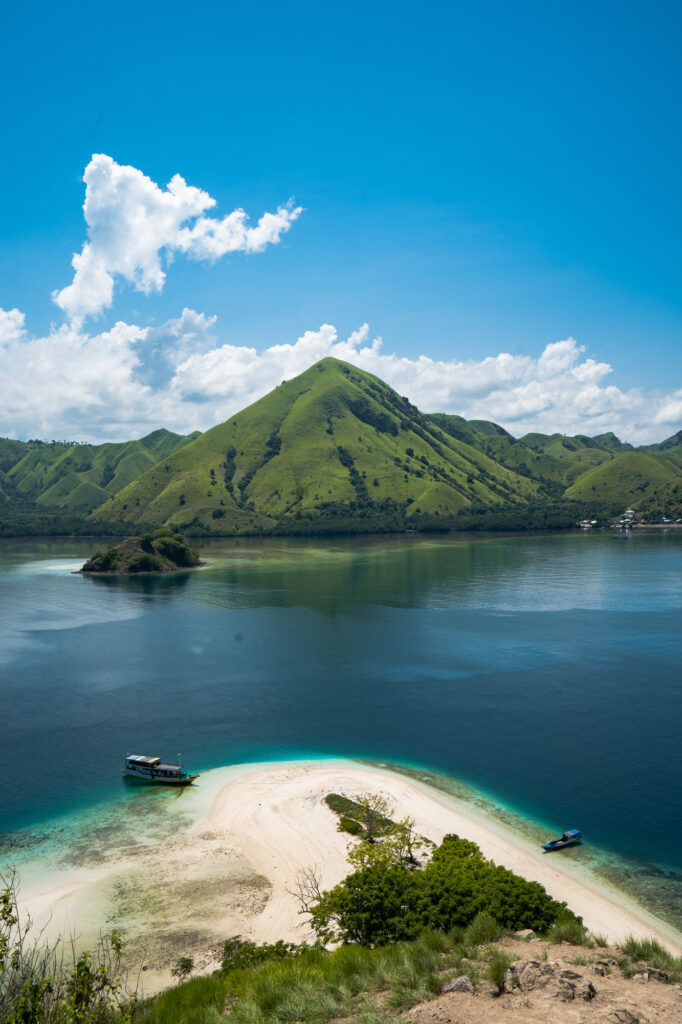 View from a hilltop over a white sand spit with vessels and a green island beyond