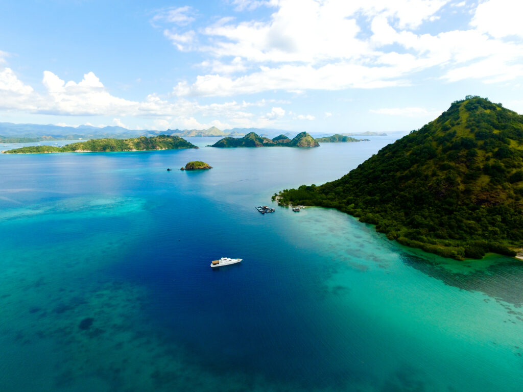 Vessel anchored off a green island and shallow reef among scattered Flores islets