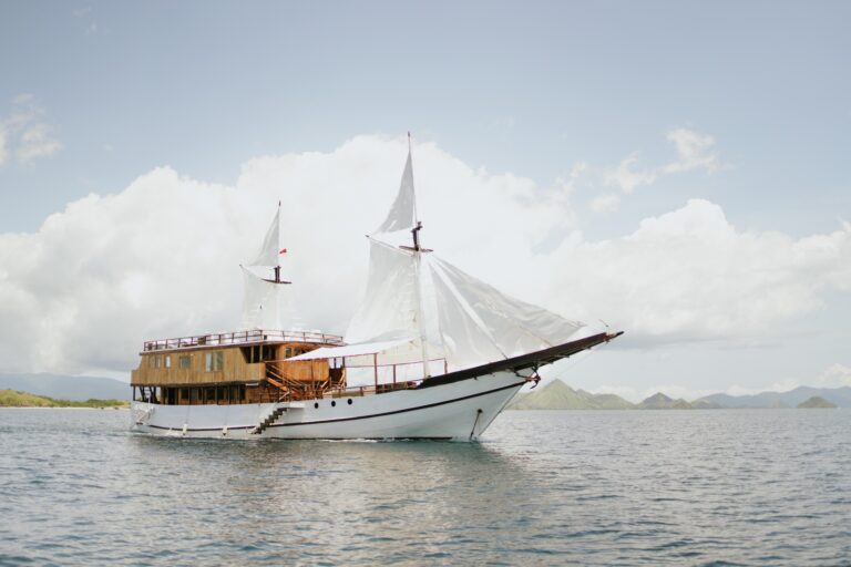 Zada Nara Komodo liveaboard cruising under sail across calm water near green hills